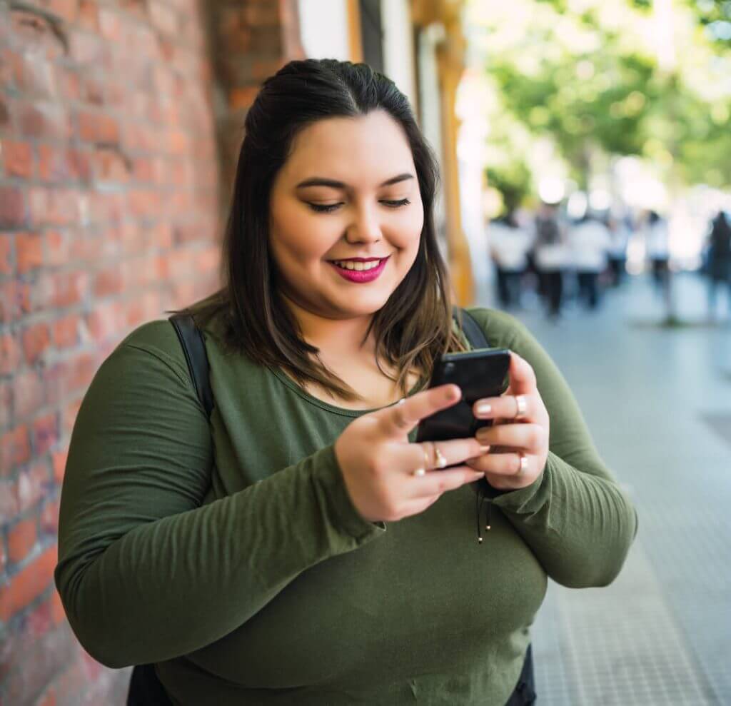 PCOS Sisters a smiling, obese woman is checking her phone.