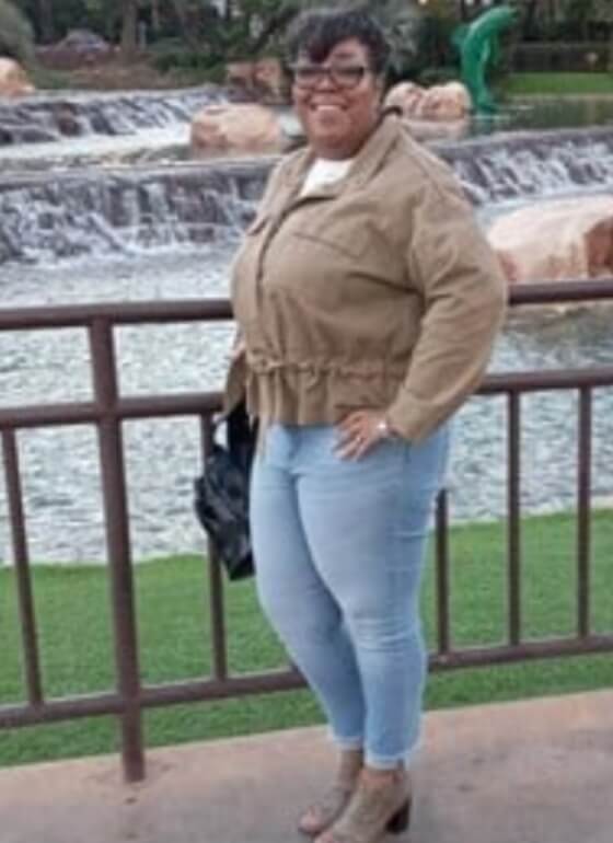 PCOS Sisters A woman in jeans and a jacket standing in front of a waterfall her Weight Loss Journey PCOS.