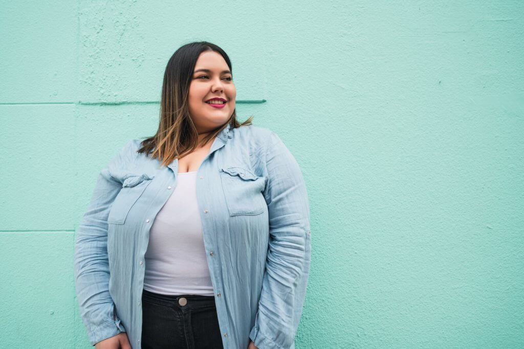 A woman standing in front of a wall wearing jeans.