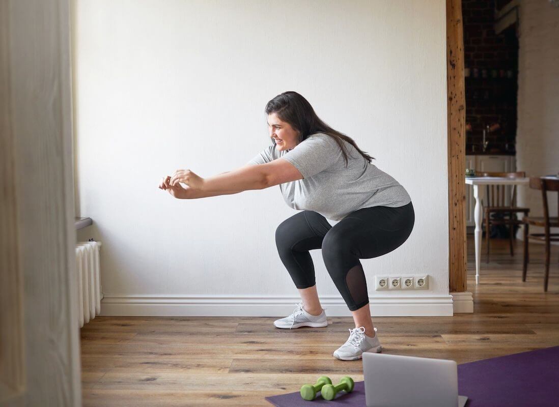PCOS Sisters A woman doing squats in front of a laptop to help with weight loss.