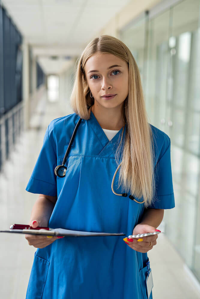 PCOS Sisters A female nurse standing in a hallway, demonstrating how it works while holding a clipboard.